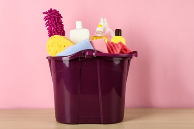 Photo of Bucket with different cleaning supplies on wooden floor near pink wall