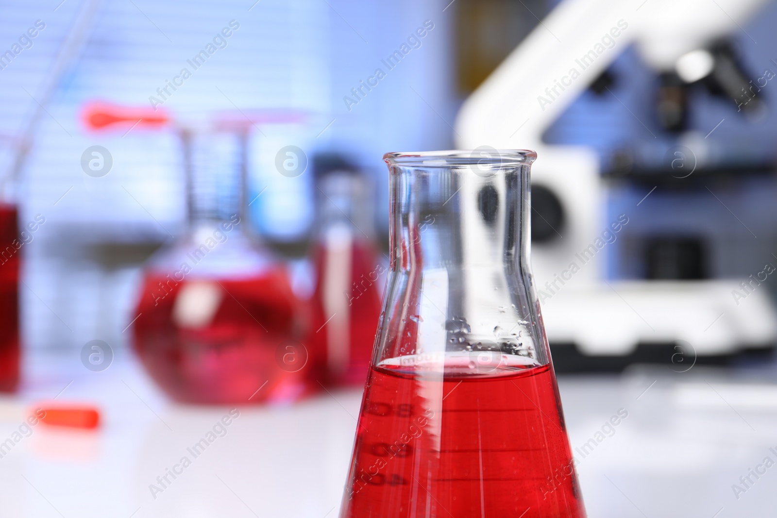 Photo of Laboratory analysis. Glass flask with red liquid on white table indoors, closeup