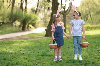 Photo of Easter celebration. Cute little girls with bunny ears holding wicker baskets outdoors, space for text