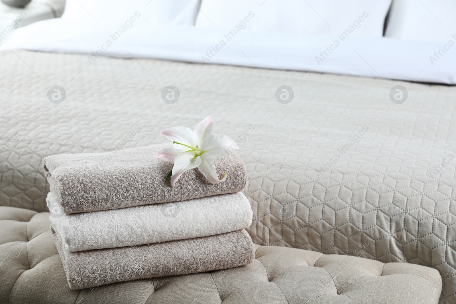 Photo of Stack of fresh towels with flower on soft bench in bedroom. Space for text