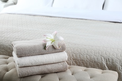 Stack of fresh towels with flower on soft bench in bedroom. Space for text