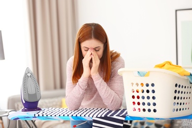 Photo of Tired housewife with clothes prepared for ironing at home