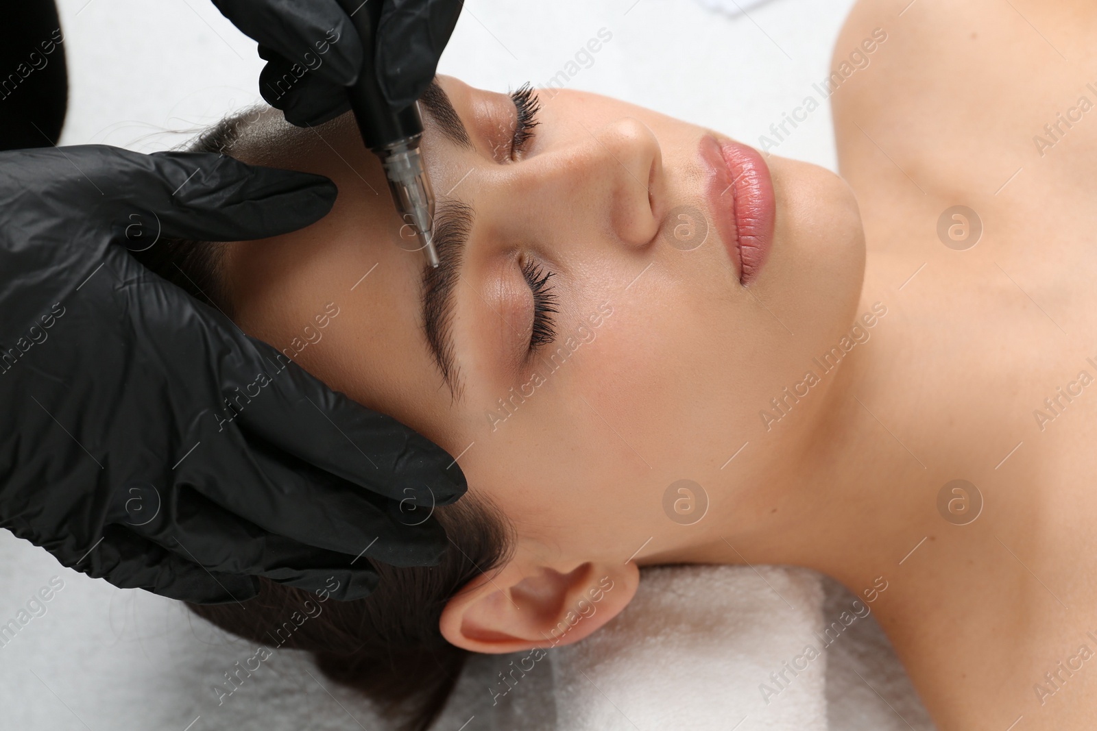 Photo of Beautician making permanent eyebrow makeup to young woman, closeup