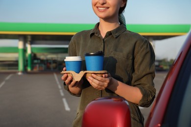 Photo of Young woman with coffee near car at gas station, closeup
