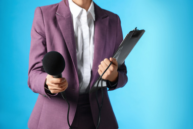 Photo of Professional journalist with clipboard and microphone on light blue background, closeup. Space for text