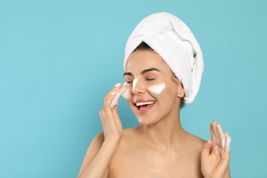 Photo of Happy young woman washing face with cosmetic product on light blue background, space for text
