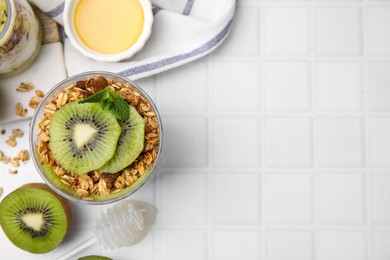 Photo of Delicious dessert with kiwi, muesli and fresh cut fruit on white table, flat lay. Space for text