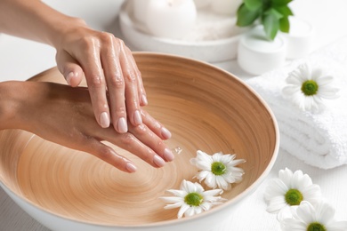 Photo of Woman soaking her hands in bowl of water and flowers on table, closeup with space for text. Spa treatment