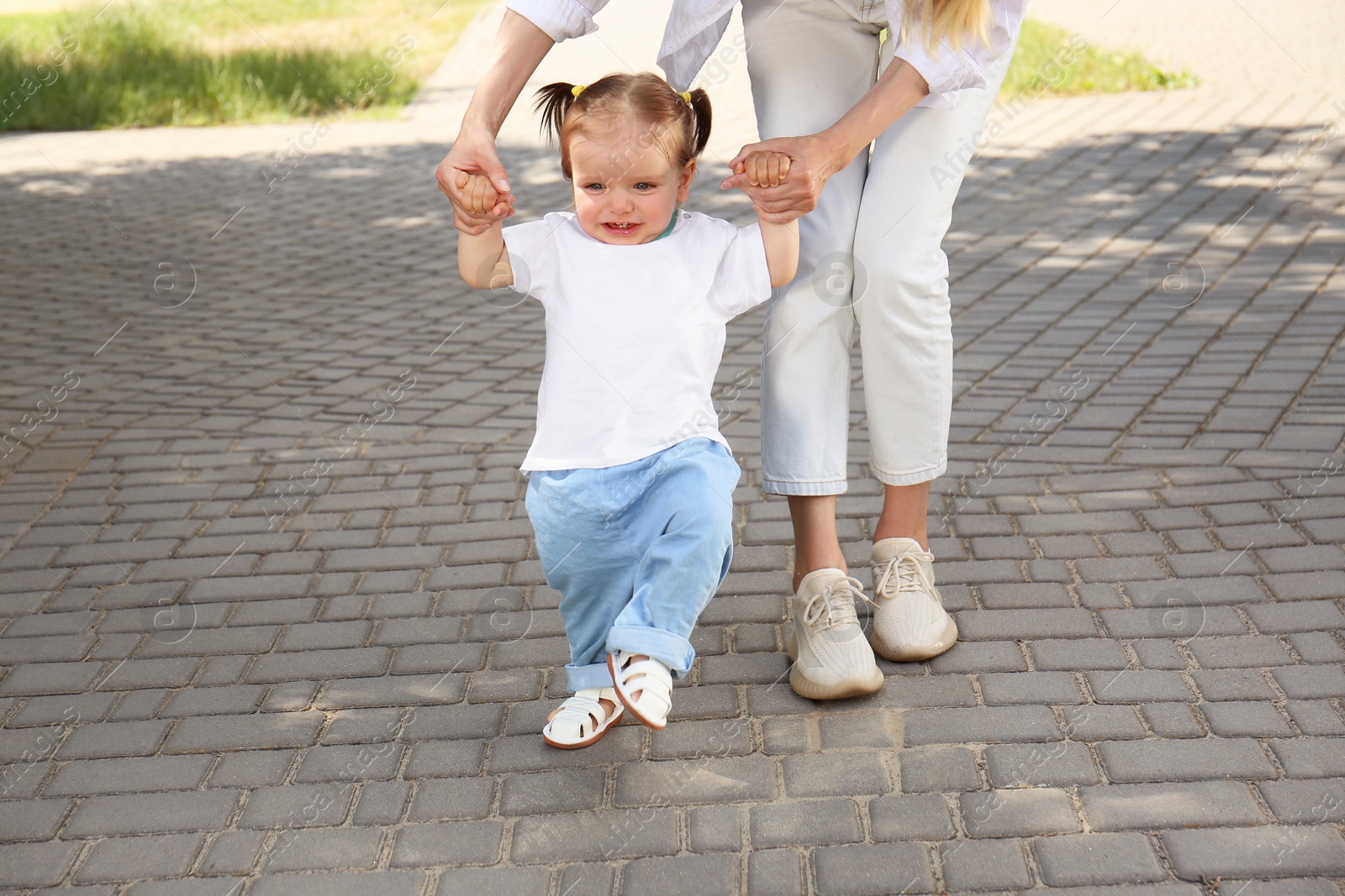 Photo of Mother supporting daughter while she learning to walk outdoors, closeup