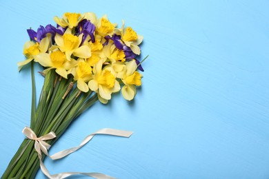 Photo of Bouquet of beautiful yellow daffodils and iris flowers on light blue wooden table, top view. Space for text