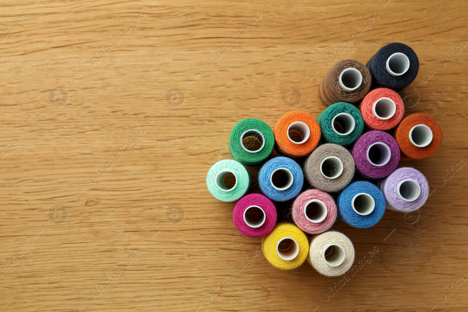 Photo of Many colorful sewing threads on wooden table, flat lay. Space for text