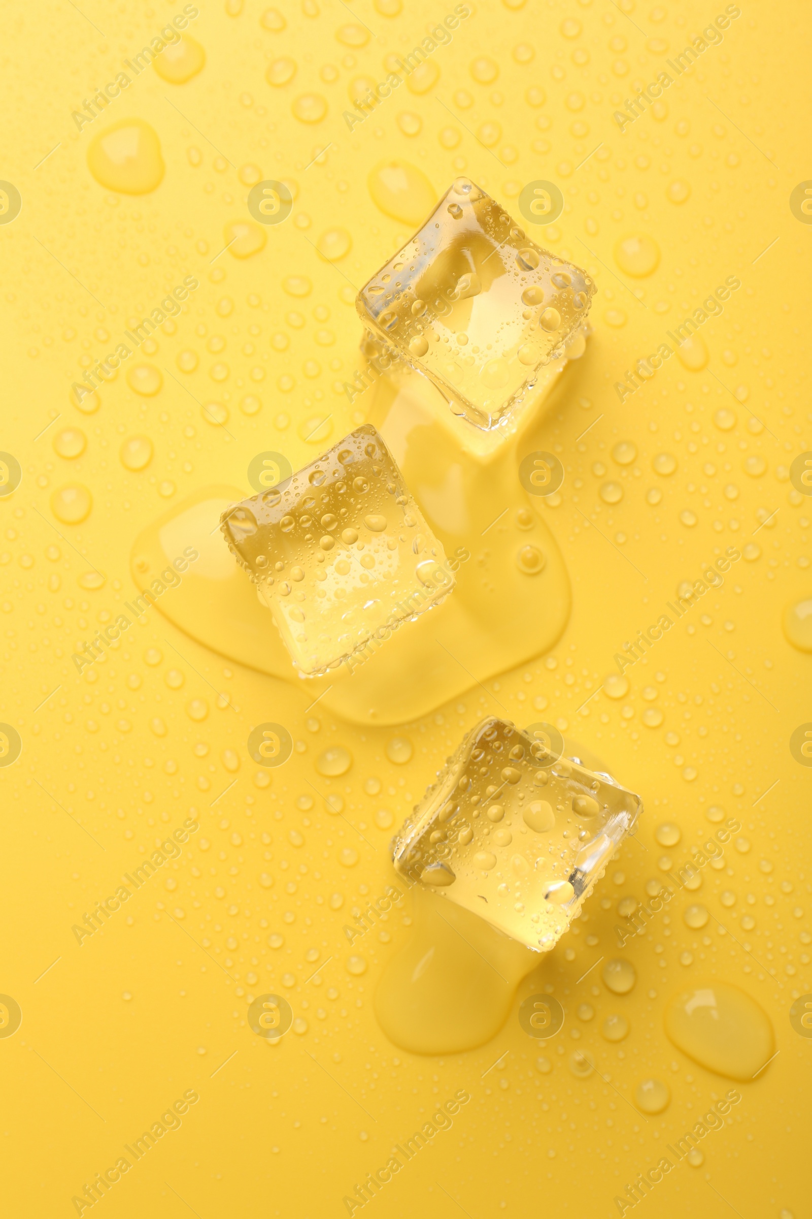 Photo of Crystal clear ice cubes on yellow background, flat lay