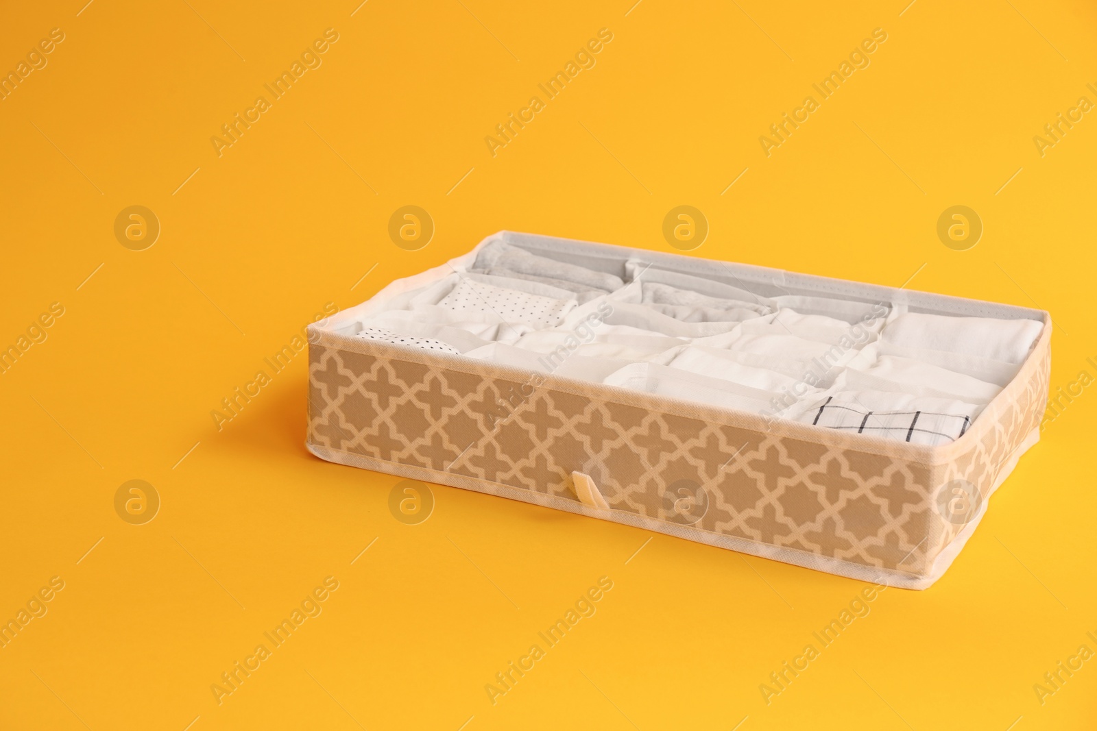 Photo of Textile organizer with folded clothes on yellow background