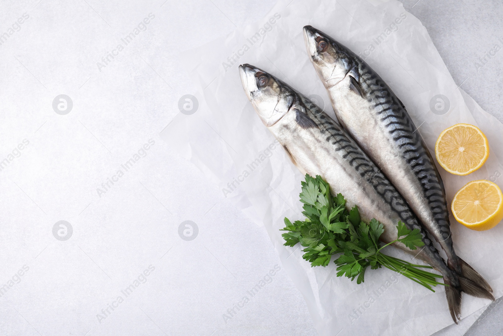 Photo of Tasty salted mackerels, parsley and cut lemons on light table, top view. Space for text