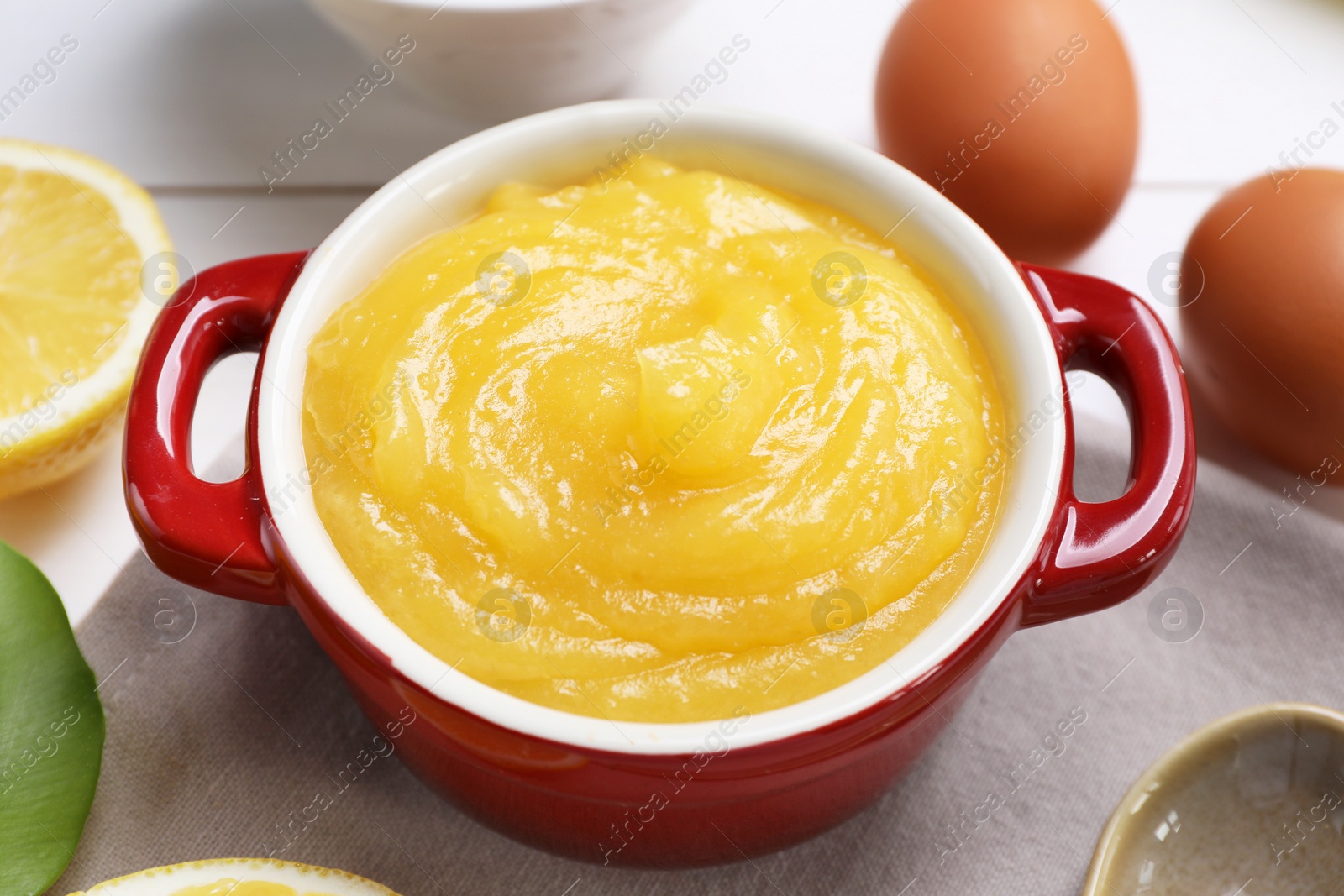 Photo of Delicious lemon curd in bowl and ingredients on table, closeup