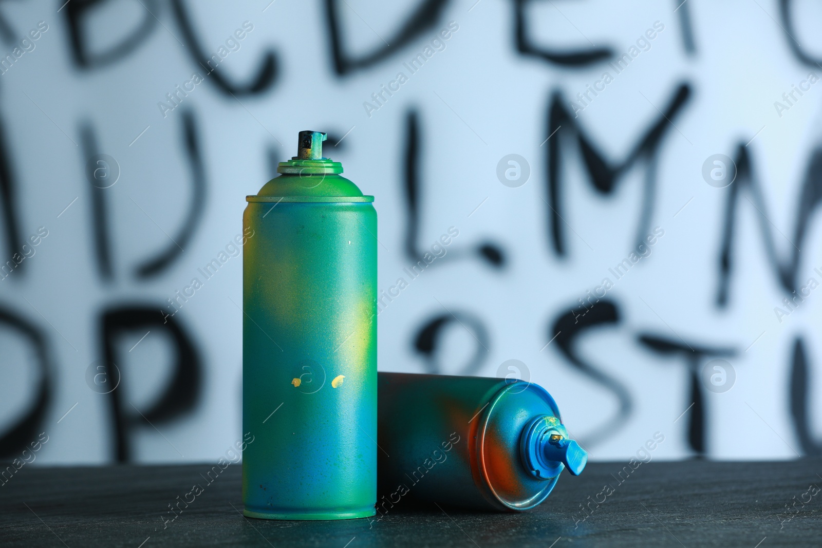 Photo of Two spray paint cans on black surface against white wall with different drawn symbols