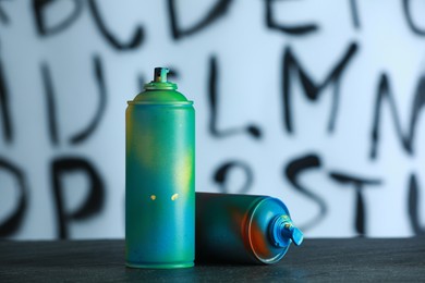 Two spray paint cans on black surface against white wall with different drawn symbols