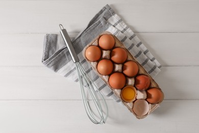 Fresh raw chicken eggs and whisk on white wooden table, flat lay