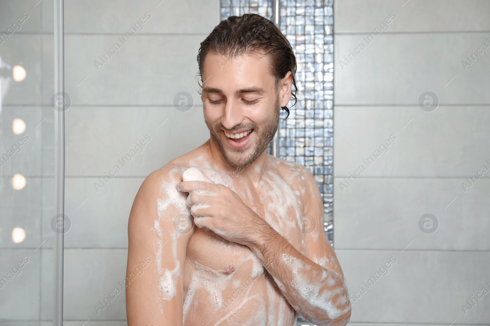 Photo of Attractive young man taking shower with soap in bathroom