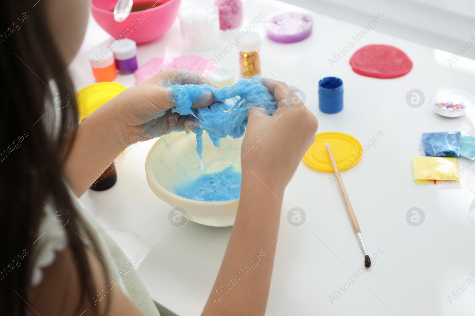 Photo of Little girl making DIY slime toy at table, closeup