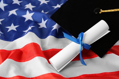 Photo of Black graduation hat and diploma on American flag, closeup. Space for text