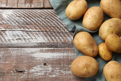 Photo of Raw fresh potatoes and napkin on wooden table, top view. Space for text