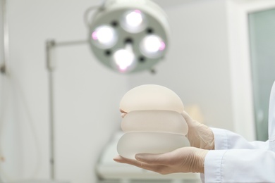 Photo of Doctor holding silicone implants for breast augmentation in clinic, space for text. Cosmetic surgery