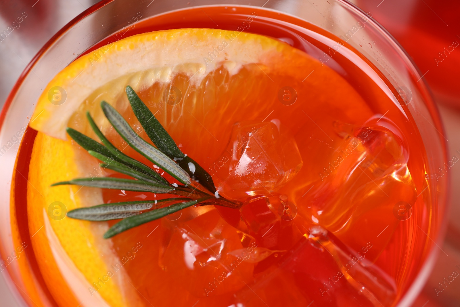 Photo of Aperol spritz cocktail, ice cubes, rosemary and orange slices in glass, closeup