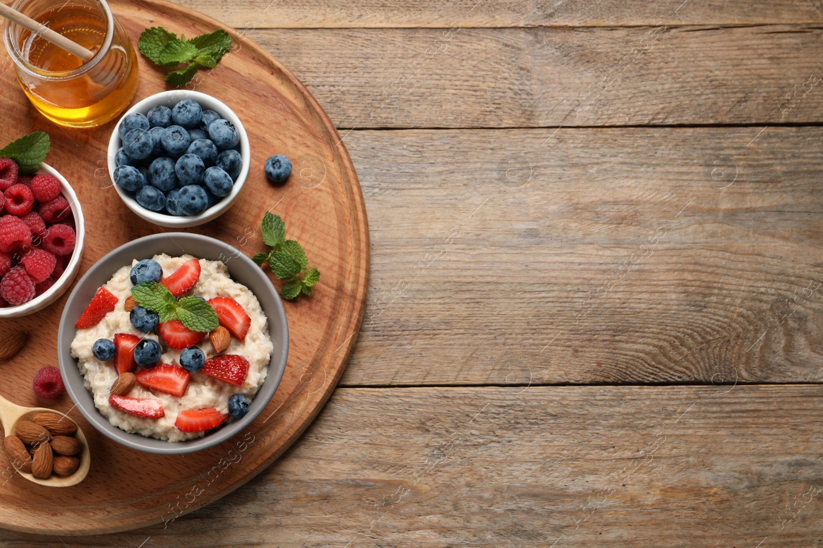 Photo of Tasty oatmeal porridge with berries and almond nuts served on wooden table, top view. Space for text