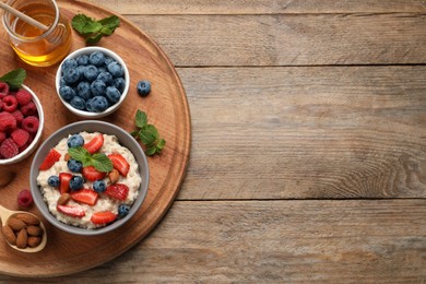 Photo of Tasty oatmeal porridge with berries and almond nuts served on wooden table, top view. Space for text