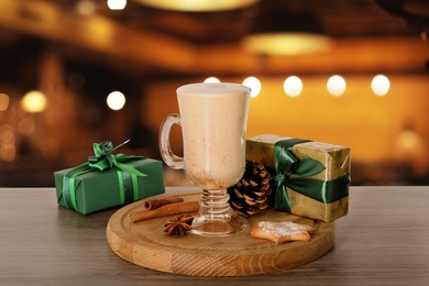 Glass of delicious eggnog, spices, cookie and gift boxes on wooden table in bar