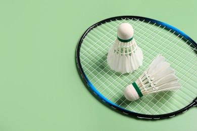 Feather badminton shuttlecocks and racket on green background, above view. Space for text
