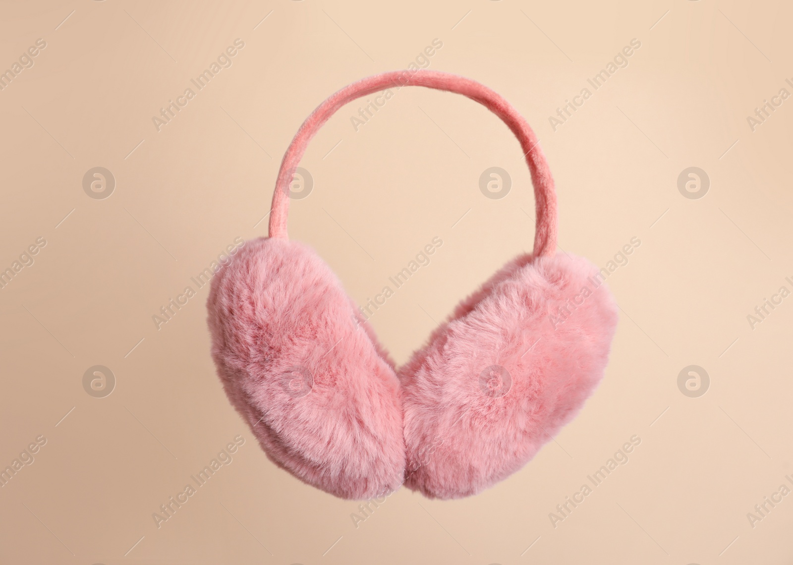 Photo of Fluffy earmuffs on beige background. Stylish winter accessory