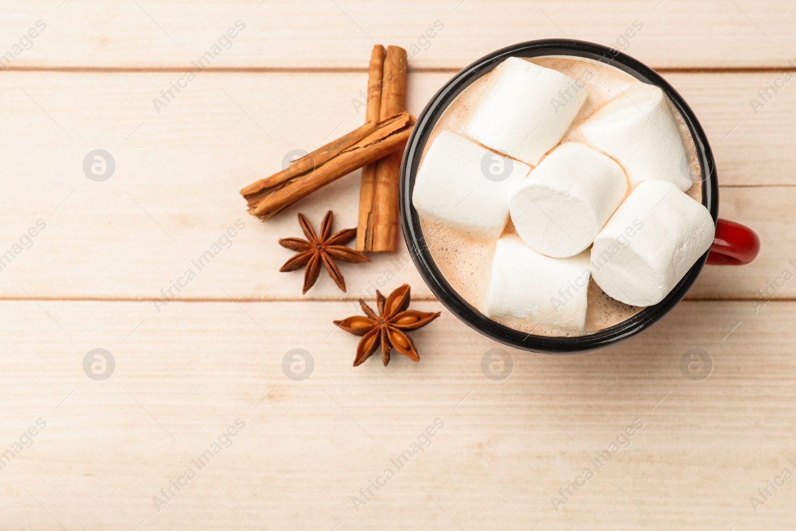 Photo of Tasty hot chocolate with marshmallows and spices on light wooden table, flat lay. Space for text