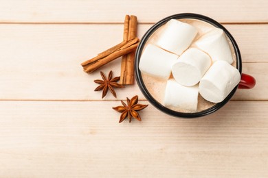 Tasty hot chocolate with marshmallows and spices on light wooden table, flat lay. Space for text