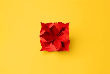 Origami art. Handmade red paper flower on yellow background, top view