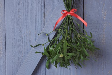 Photo of Mistletoe bunch with red bow hanging on grey wooden wall. Traditional Christmas decor