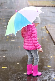 Photo of Little girl with umbrella splashing in puddle on rainy day. Autumn walk