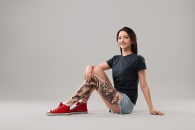 Smiling tattooed woman posing on grey background