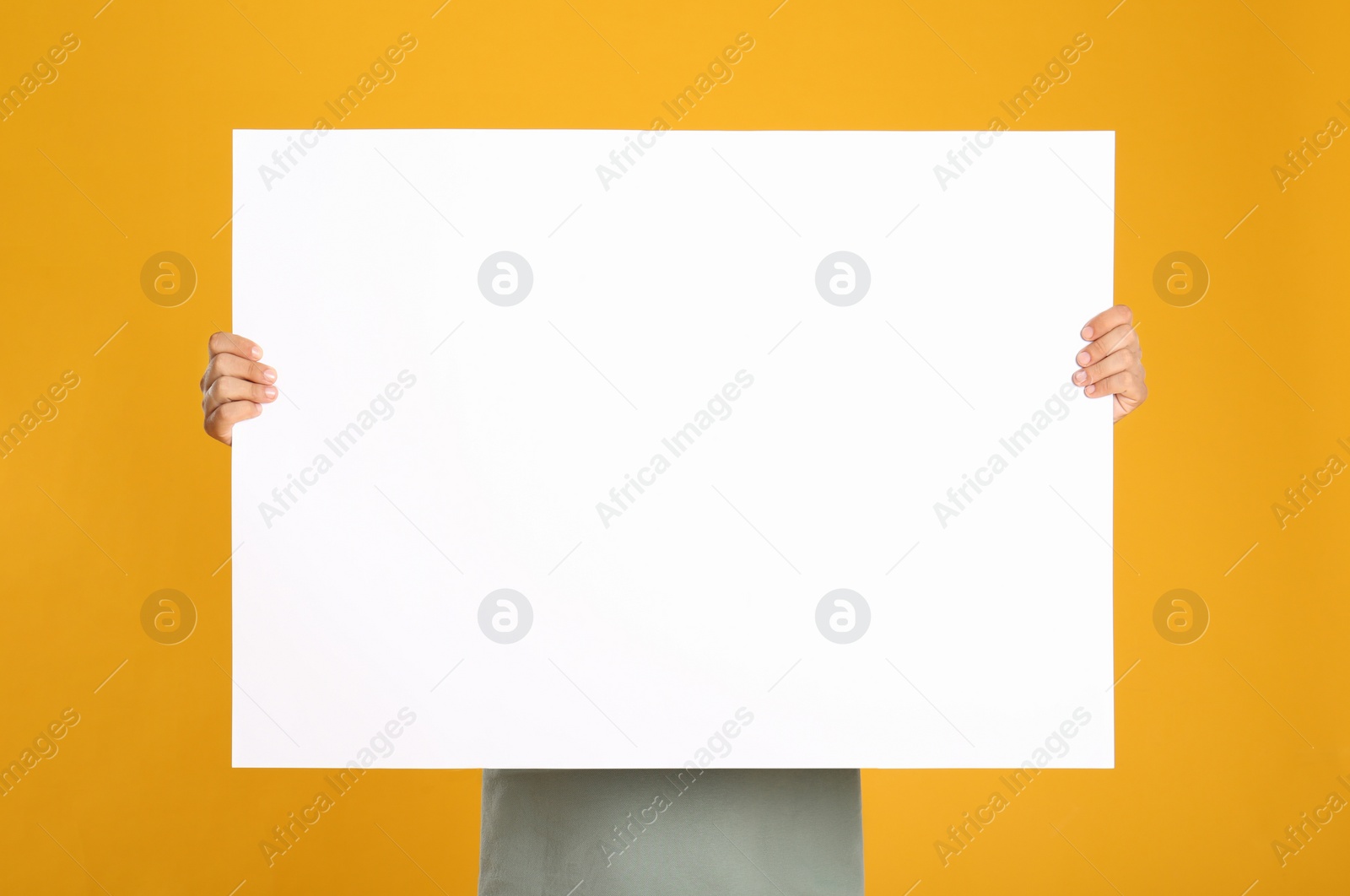 Photo of Man holding white blank poster on yellow background. Mockup for design