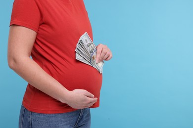 Photo of Surrogate mother. Pregnant woman with dollar banknotes on light blue background, closeup. Space for text