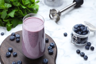 Glass of blueberry smoothie with mint and fresh berries on white marble table. Space for text