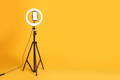 Photo of Modern tripod with ring light and smartphone on yellow background. Space for text