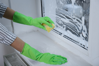 Woman cleaning window with sponge indoors, closeup