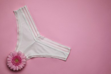 Photo of Woman's panties and gerbera flower on pink background, top view. Space for text