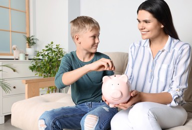 Boy with his mother putting coin into piggy bank at home