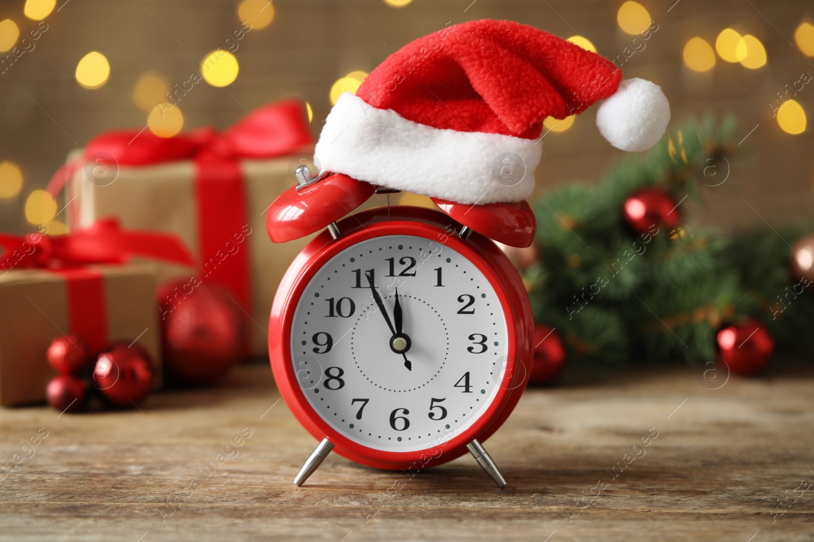 Photo of Alarm clock with decor on wooden table against blurred Christmas lights, closeup. New Year countdown