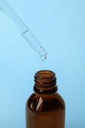 Photo of Dropping cosmetic oil from pipette into bottle on light blue background, closeup