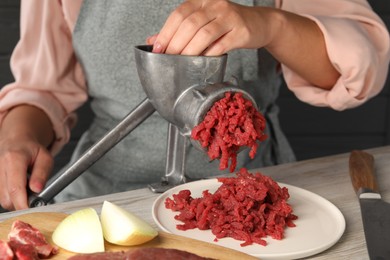 Woman making beef mince with manual meat grinder at light wooden table, closeup