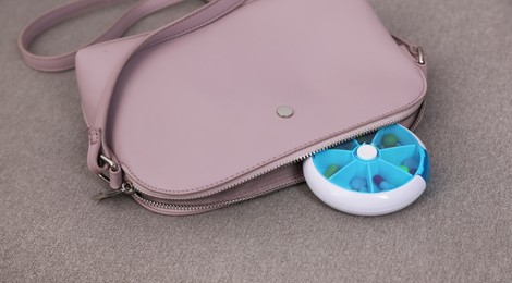 Pill box with medicaments near stylish women's bag on sofa, closeup